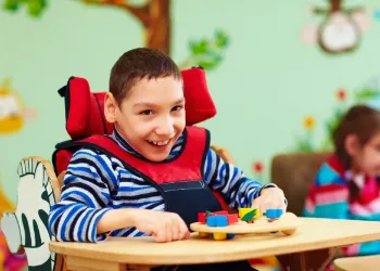 Child in wheelchair smiling and playing with blocks.
